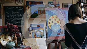 Rear view of Young painter girl in apron painting still life picture on canvas in art-class