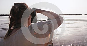 Rear view young photographer woman taking pictures of happy mother and daughter at golden sunrise sea beach slow motion.