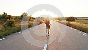 Rear view of young sportsman jogging on a country road during sunset