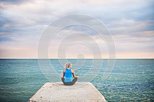 Rear view of a young sporty woman doing yoga exercise by the ocean outside.