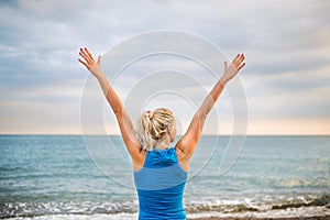 Rear view of young sporty woman runner in blue sportswear standing on the beach.