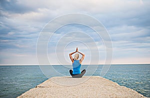 Rear view of a young sporty woman doing yoga exercise by the ocean outside. photo