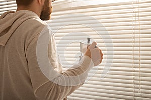 Rear view of young stylish man peeking through hole in window blinds and looking out into street. Concept of enjoying