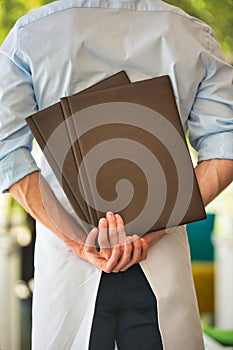 Rear view of young waiter holding menus while standing at restaurant