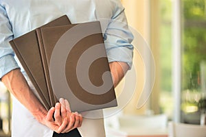 Rear view of young waiter holding menus while standing at restaurant