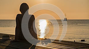 Rear view of a young woman admiring the dawn of the sea, in the distance a ship is visible. Romance and travel concept