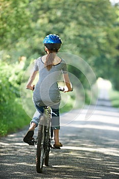 Rear View Of Young Woman Cycling On Country Lane