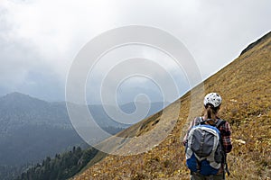 Rear view of young woman hiker in cap with large hiking backpack looking at the mountain view of the Aibga ridge of the Caucasus