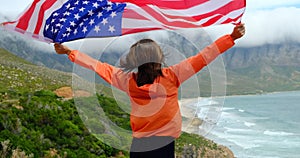 rear view of young woman holding american flag in front of sea, independence day