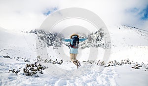 Rear view of young woman jumping in snowy winter nature, arms stretched.