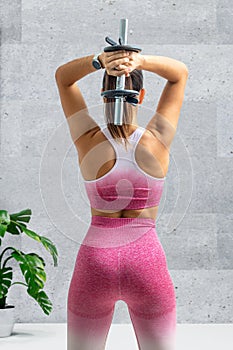 Rear view of young woman lifting dumbbell above shoulder