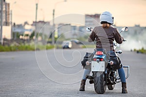 Rear view at young woman motorcyclist ready to stard riding on motorcycle on asphalt road, copy space