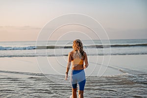 Rear view of young woman running on beach, morning routine and healthy lifestyle concept.