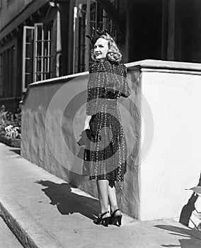 Rear view of a young woman standing in front of a wall looking over her shoulder