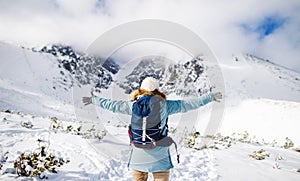 Rear view of young woman standing in snowy winter nature, arms stretched.