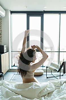 Rear view of young woman stretching in bed after wake up in morning with sunlight