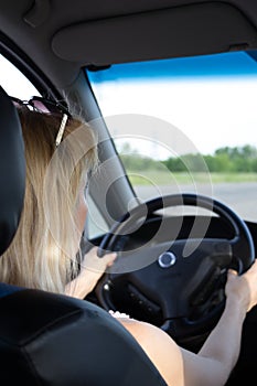 Rear view of young woman in summer wear looking on road through the windshield while driving a car