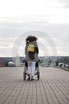 Rear view of young woman walking with disabled man in wheelchair on the quay