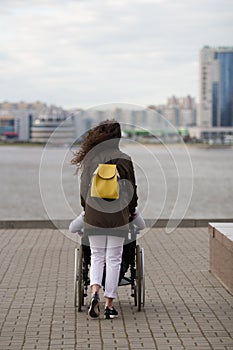 Rear view of young woman walking with disabled man in wheelchair on the quay