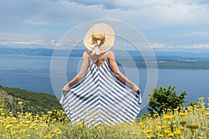 Rear view of young woman wearing striped summer dress and straw hat standing in super bloom of wildflowers, relaxing