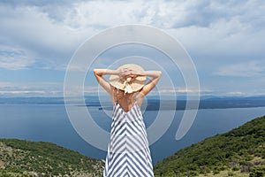 Rear view of young woman wearing striped summer dress and straw hat standing in super bloom of wildflowers, relaxing