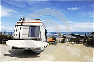 Rear of vintage camper parked on the beach seaside with a surfboard on back - Leisure trip in the summer