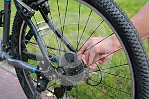 Rear wheel of a bicycle and hands of a man outdoors in the park. Bike repair and maintenance
