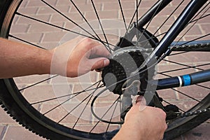 Rear wheel of a bicycle and male hands on a tiled road. Bicycle wheel repair.