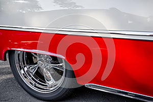 Rear wheel with chrome rim under a low quarter of a red and white vintage retro car