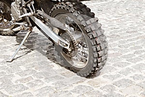 The rear wheel of an off-road motorcycle against the background of a stone pavement. Motorbike parked at empty cobblestone road. E