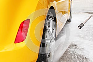 Rear wheel of yellow car being washed with jet water stream in c