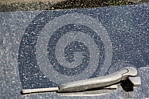 Rear window of a dirty car with a windshield wiper covered with a layer of dry dust.