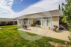 Rear Yard  Of Ranch Home With Concrete Patio With Lounge Chairs & Bench