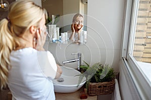 Rear on young Caucasian attractive female looking at mirror and smiling in bathroom.