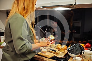 Rearview of blond unrecognizable woman cooking, spreading butter on bread buns in wooden kitchen corner. Eating disorder photo