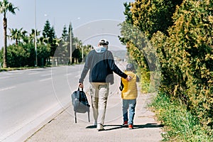 Rearview of father and son walking near city road. Dad holding his kid's back when taking a stroll in the southern