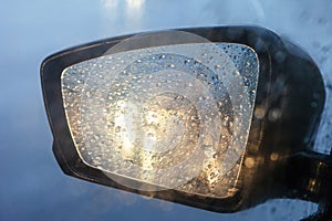 Rearview mirror with drops of water from the rain and a car with headlights. Selective focus, shallow DOF