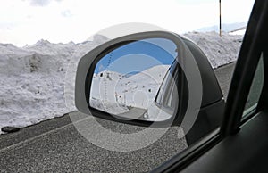 Rearview mirror of the passenger car on the mountain road in winter with snow and reflection