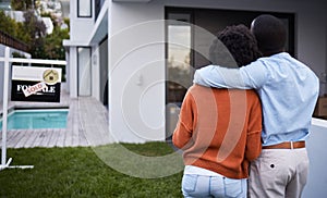 This dream home is finally ours. Rearview shot of a young couple standing outside their new home.