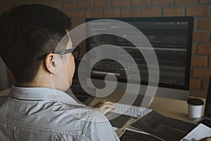 Rearview of the software developer is working on a computer keyboard and analyzing the code written in the program on the computer