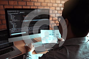 Rearview of the software developer is working on a computer keyboard and analyzing the code written in the program on the computer