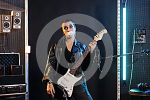 Rebel artist with grunge jacket holding electric guitar while playing rock music in sound studio