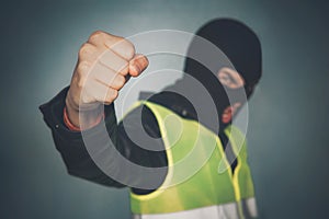 Rebellious protester in a mask shows his fist. Yellow Vest protest. street riots. French revolution. Angry thug bully threatening