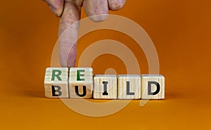 Rebuild symbol. Concept word `rebuild` on wooden cubes on a beautiful orange table. Businessman hand. Orange background. Busines