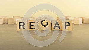 RECAP word, text written on wooden cubes on a yelllow background