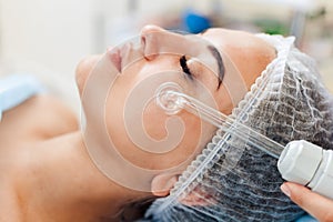 Receiving electric darsonval facial massage procedure at beauty salon.