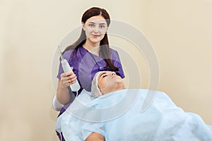 Receiving electric darsonval facial massage procedure at beauty salon.