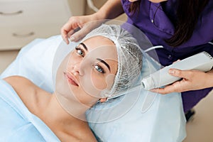 Receiving electric darsonval facial massage procedure at beauty salon.