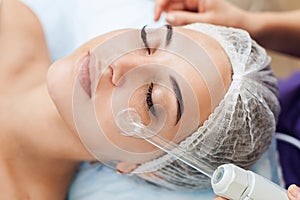 Receiving electric darsonval facial massage procedure at beauty salon.