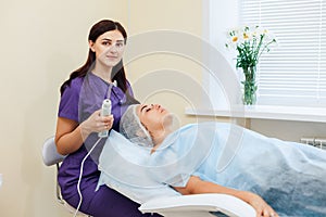 Receiving electric darsonval facial massage procedure at beauty salon.